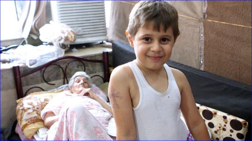 Aws, a 10-year-old Iraqi Christian boy, has spent much of his young life fleeing jihadists. Munira Aziz, 74,pictured behind him, considers herself fortunate to have escaped ISIS (photo: Benjamin Hall).